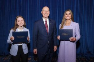 2026 delegates holding certificates, standing on stage with Pete Ricketts